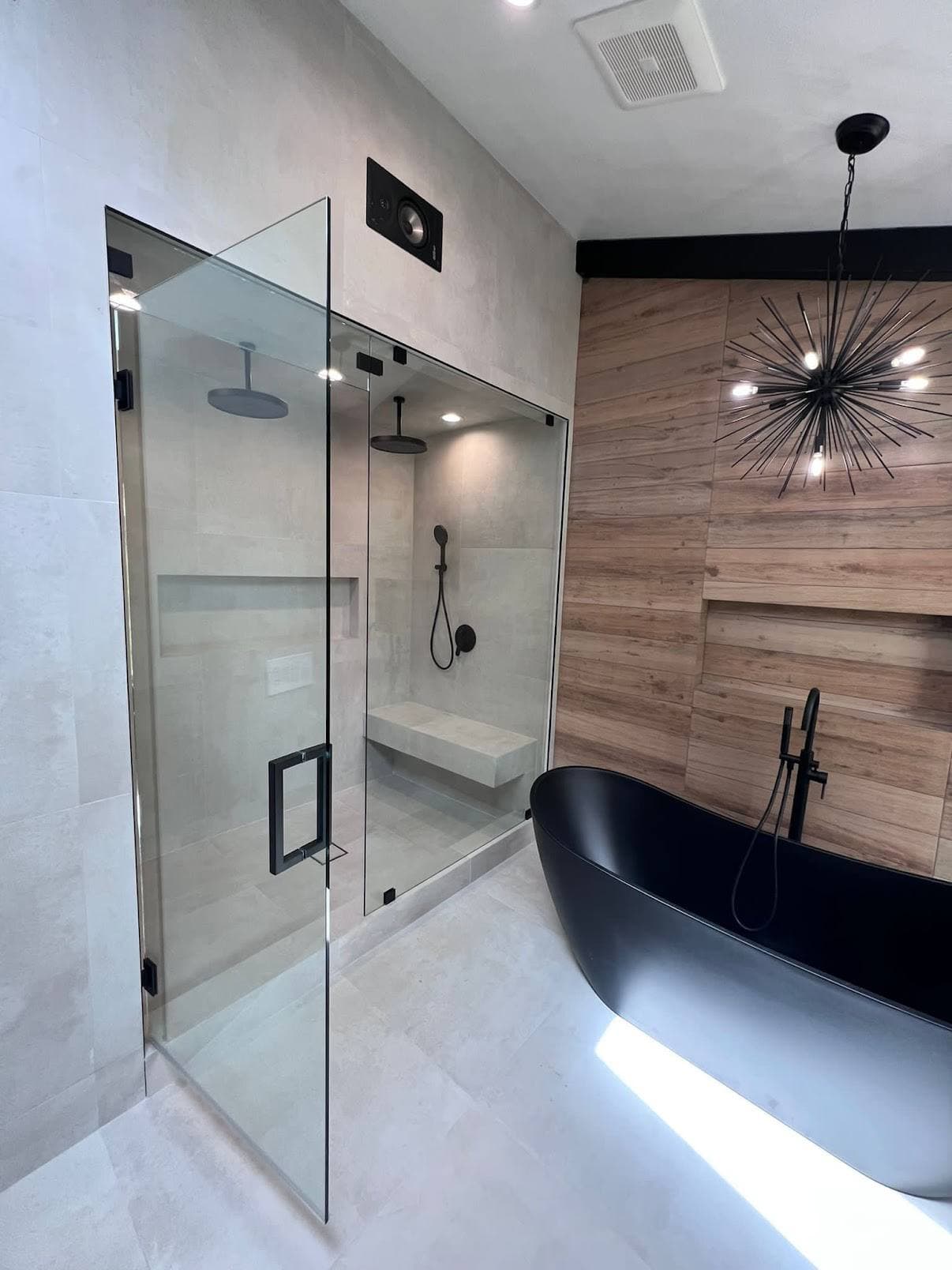 Bathroom remodel with glass shower, black tub, wood accent wall, and black fixtures