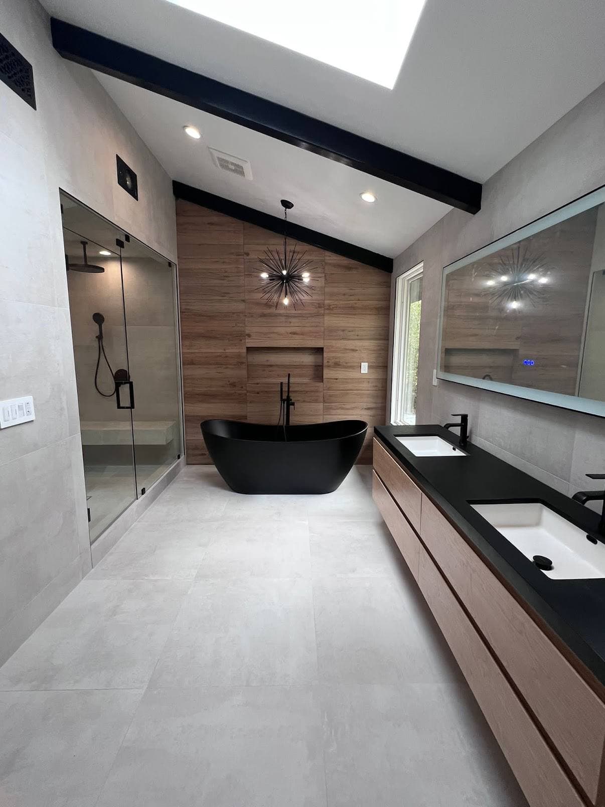 Modern bathroom with black freestanding tub, wood accent wall, double vanity, and glass shower