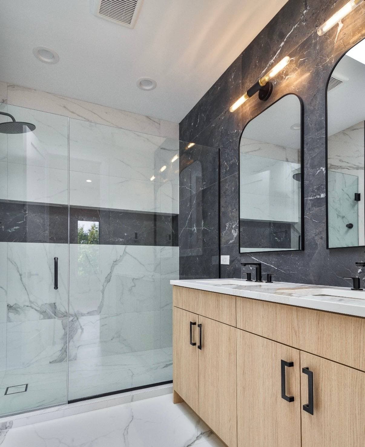 Bathroom remodel with marble-look shower walls, glass enclosure, wood vanity, and black fixtures