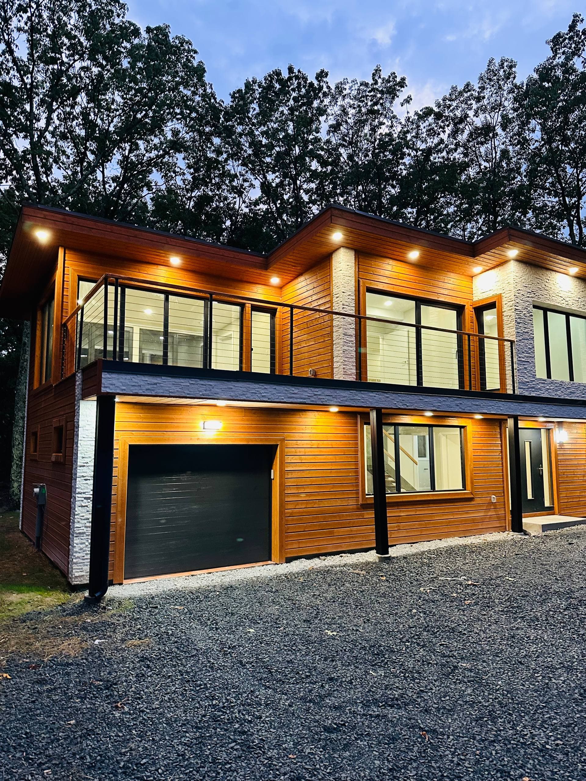 Modern wood exterior detail with balcony, warm lighting, garage, and black trim