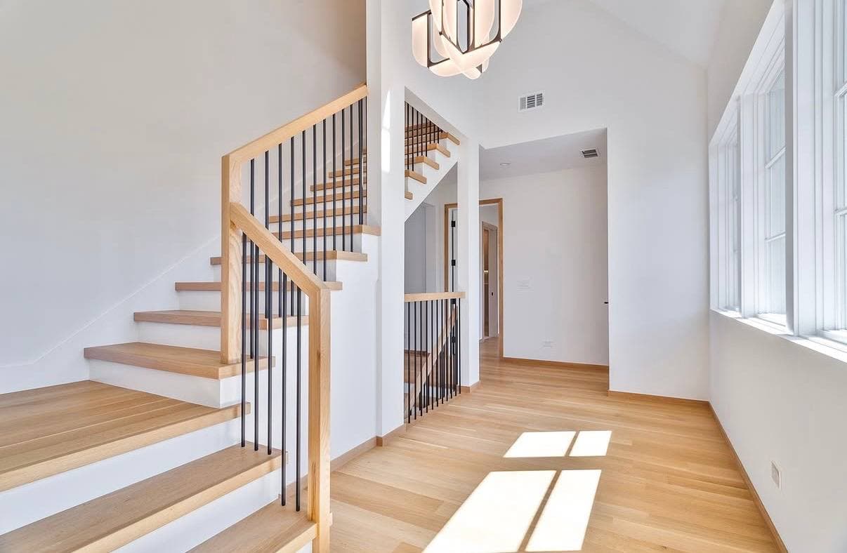 Bright interior stair hall with oak treads, wood railing, black balusters, and finished wood flooring