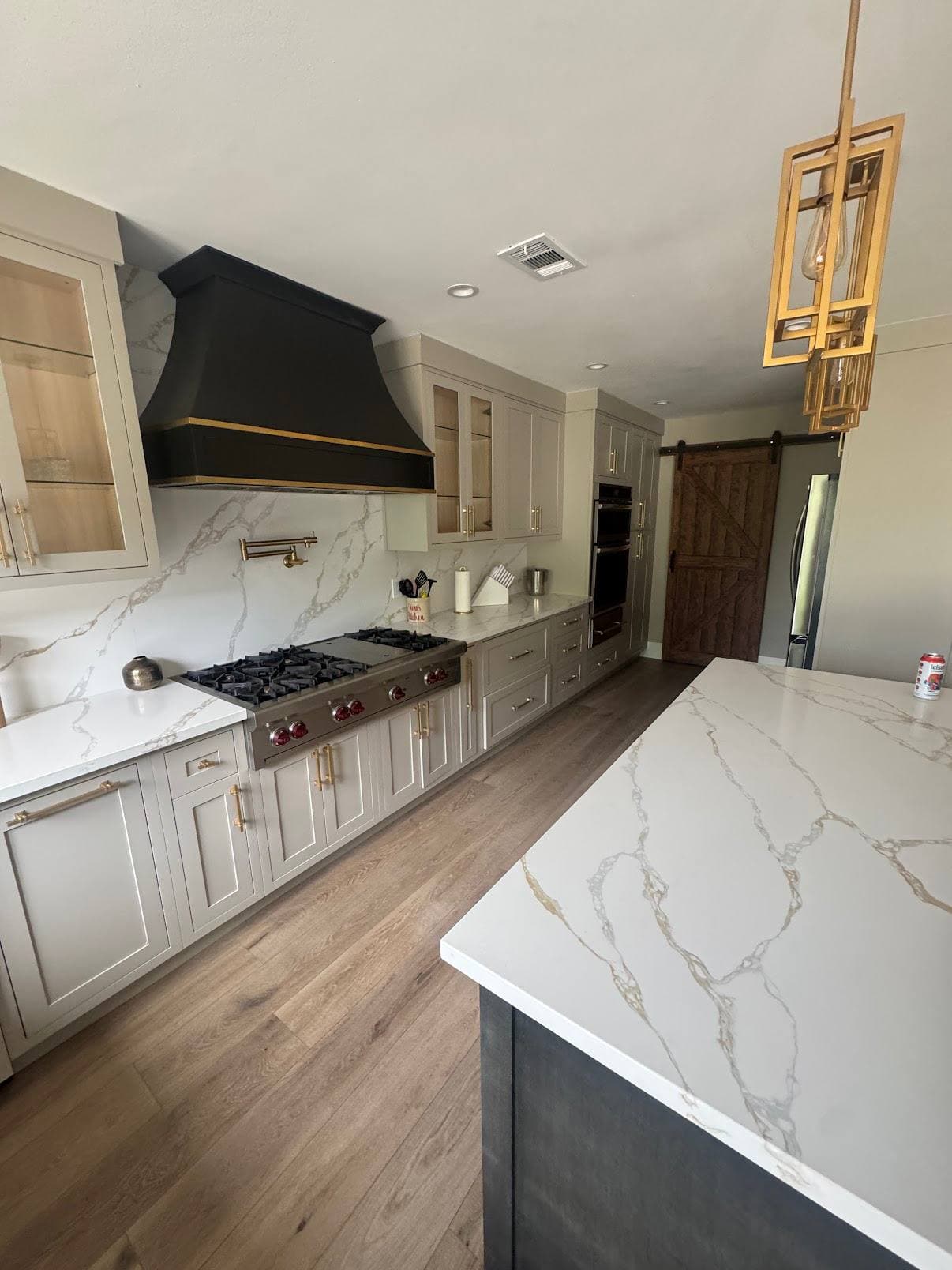 Kitchen remodel with brass range hood, marble-look backsplash, and wood barn door