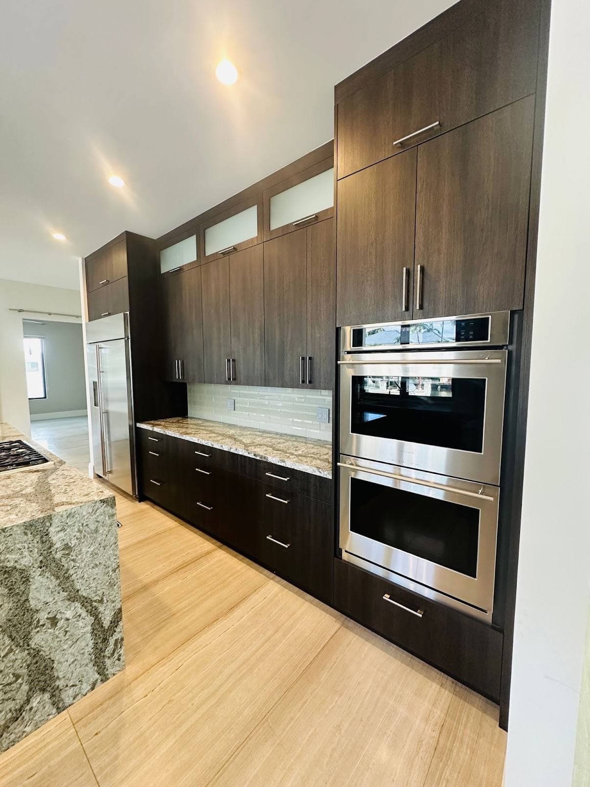 Dark kitchen cabinet wall with built-in ovens, refrigerator, and stone counters