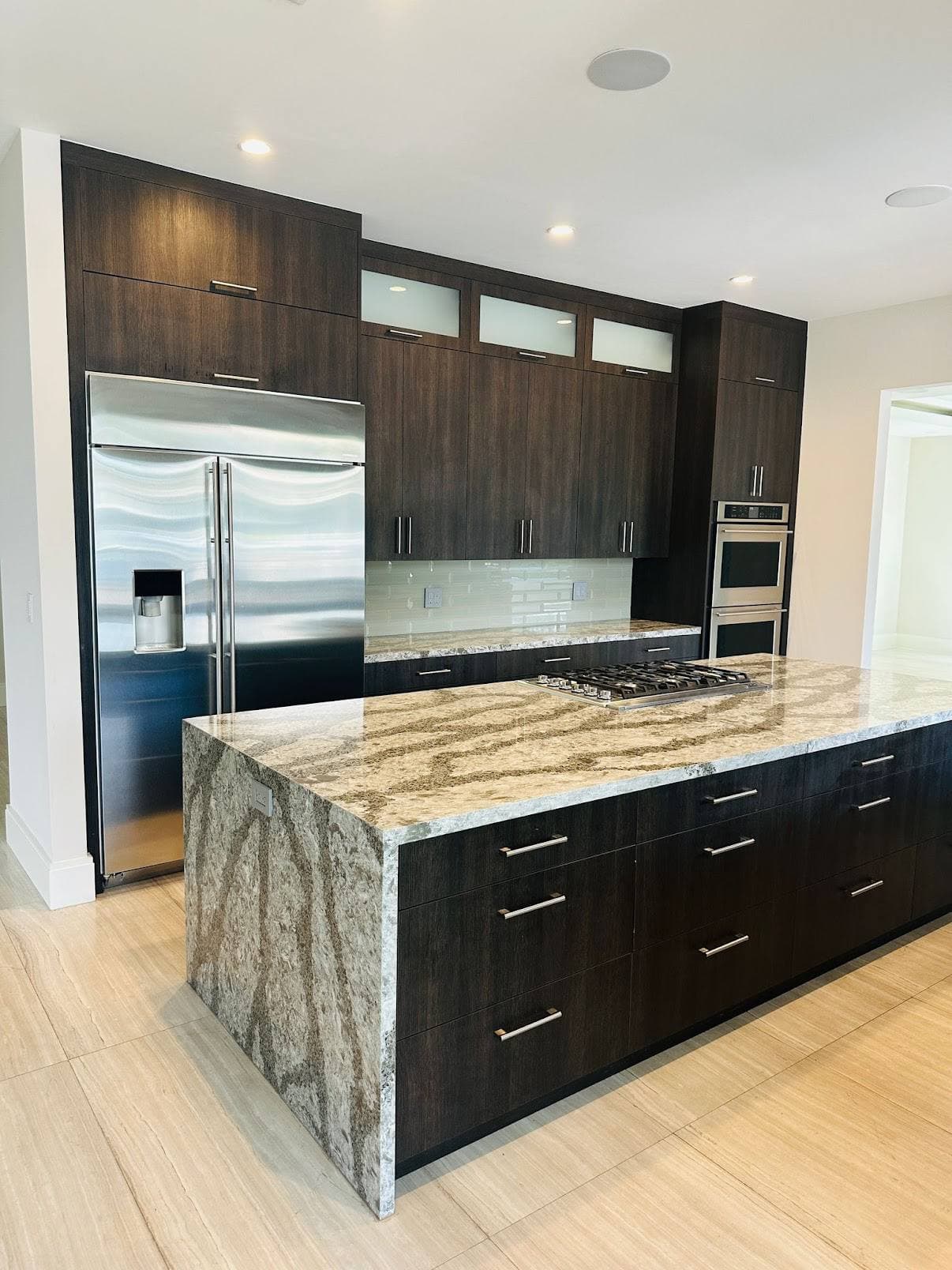 Kitchen remodel with dark cabinetry, stone waterfall island, and integrated appliances