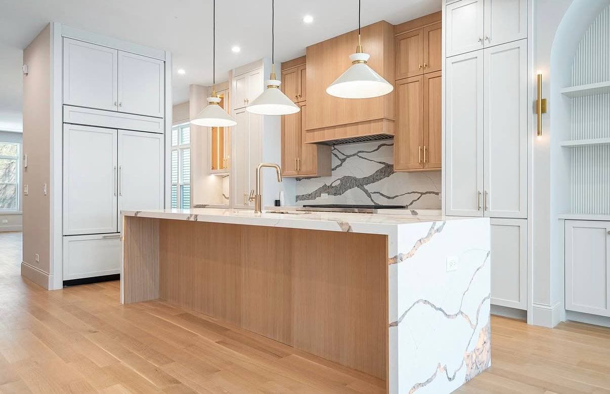 Light oak kitchen island with white cabinetry, pendant lighting, and marble-look counters