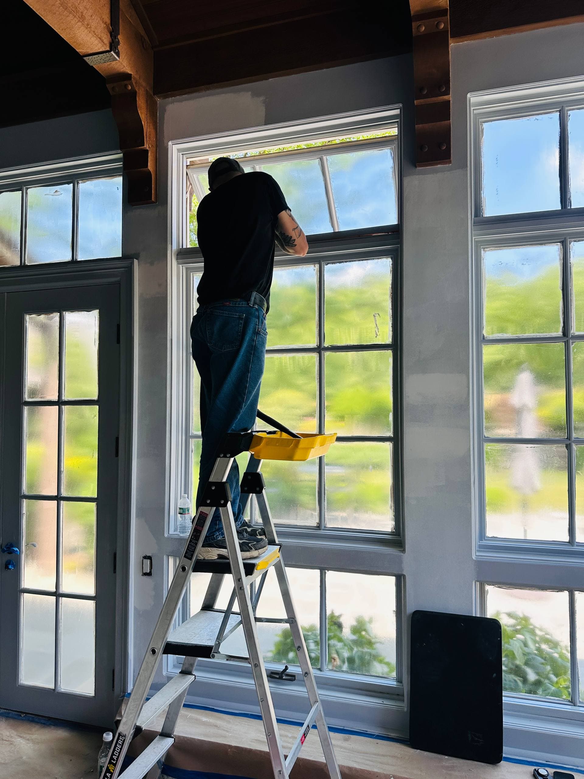 Worker finishing tall interior windows from a ladder during renovation work
